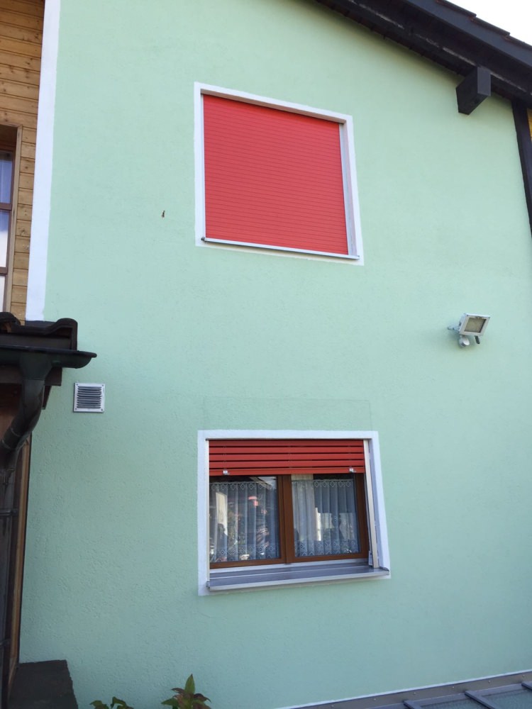 Frisch gestrichene Fassade in Mintgrün mit roten Fensterläden